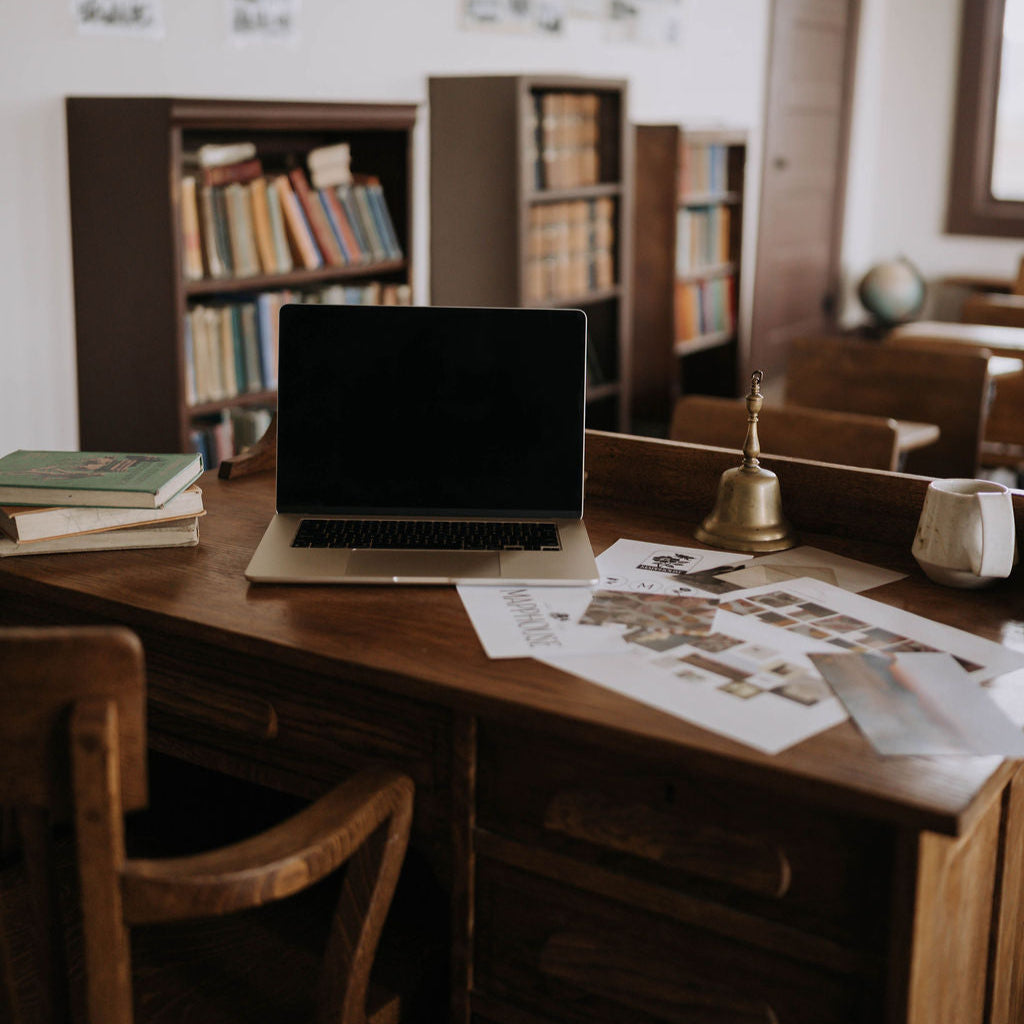 Laptop on a wooden desk with books and papers in a room setting