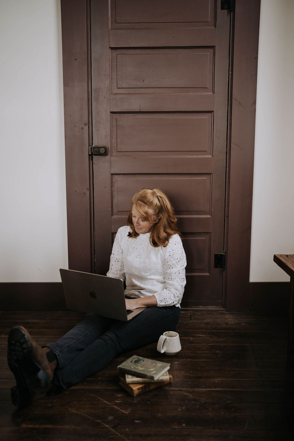 Person sitting on the floor with a laptop in front of a wooden door.